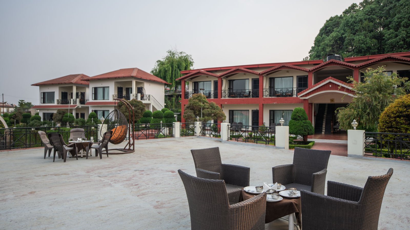 Aerial view of a sprawling luxury resort with several red-roofed stone cottages nestled on a green hillside in the Himalayas.